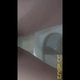 Emi hovers over a hospital toilet next to the grab bars and shits into the bowl, filmed from below. Vertical format video. Over 0.5 minutes.